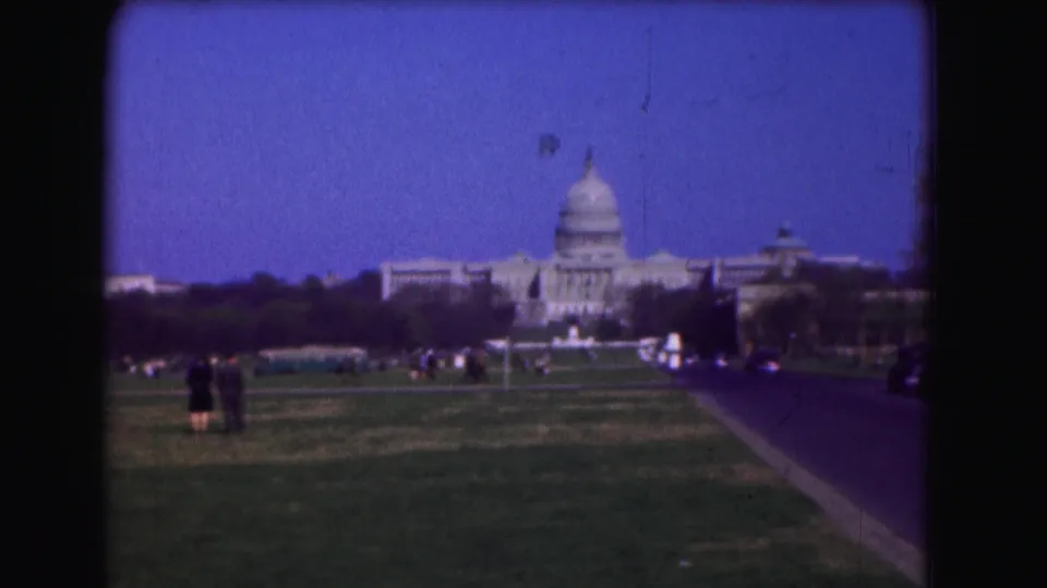 A distant 1975 view of the U.S. Capitol from the Mall, with pedestrians on the lawn and a roadway leading toward the building.