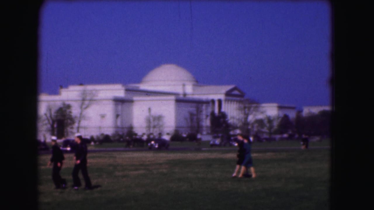 People walking across a grassy lawn with a large white domed building in the background.