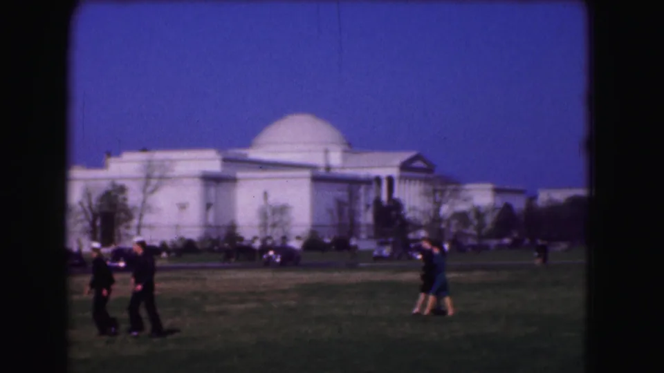 1975 Washington, DC home-movie frame showing pedestrians on a lawn before a large white domed historic building.