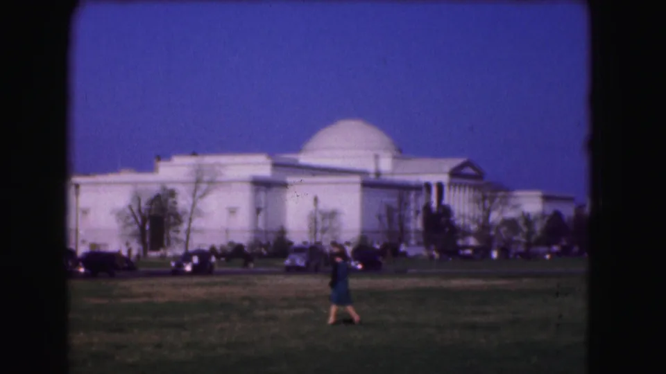 1975 Washington, DC home-movie frame showing a lone pedestrian on grass before a large white domed historic building.
