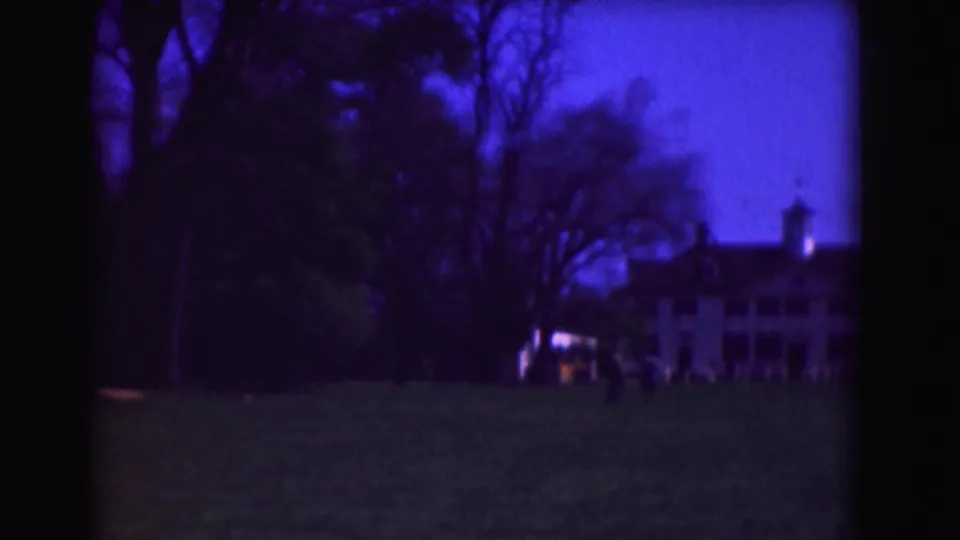 1975 Washington, DC frame with a darker handheld view across grass toward trees and a partly visible white building.