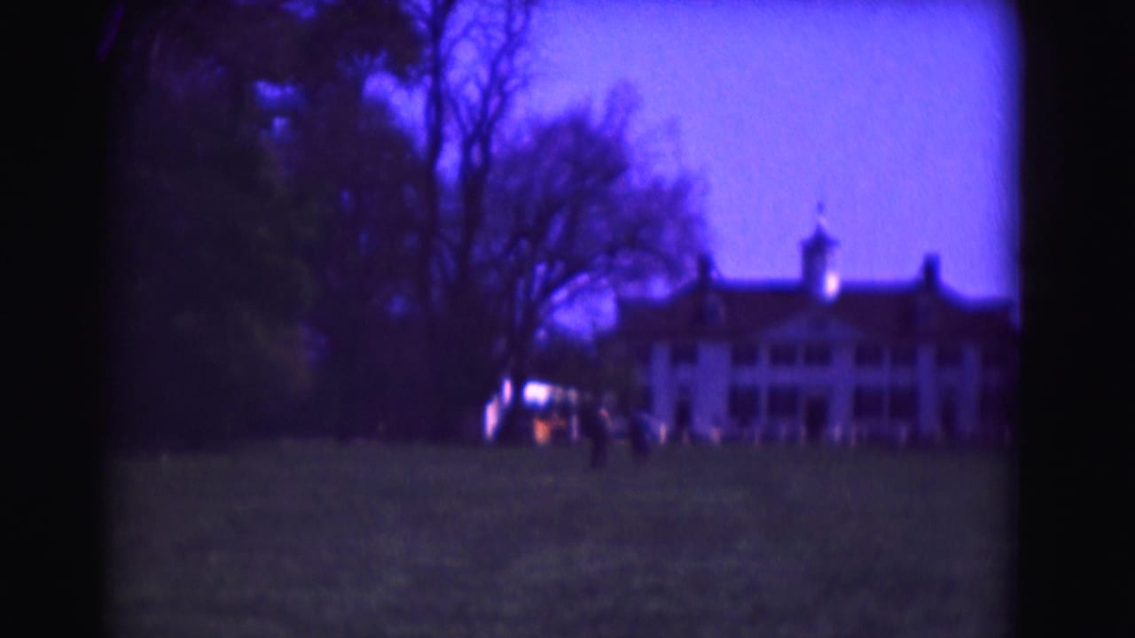 1975 Washington, DC 8mm frame showing a large white mansion-like building across a lawn, with bare trees and distant figures in purple twilight.