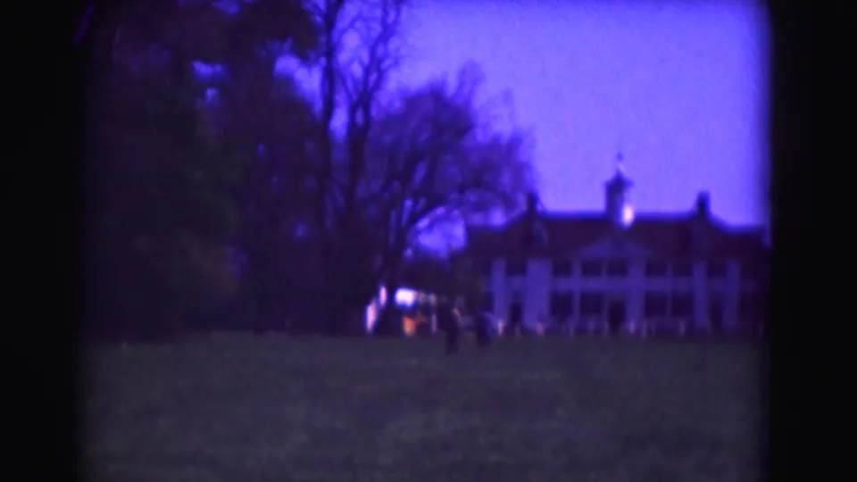 1975 Washington, DC 8mm frame showing a large white mansion-like building across a lawn, with bare trees and distant figures in purple twilight.