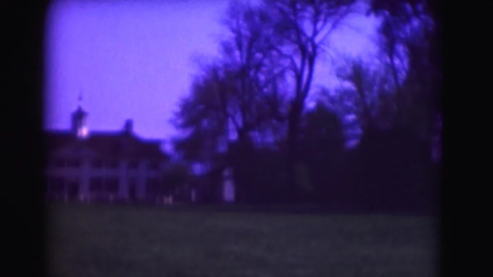 End frame from 1975 Washington, DC footage showing the grand building set back behind trees and lawn, with strong purple low-light film color.