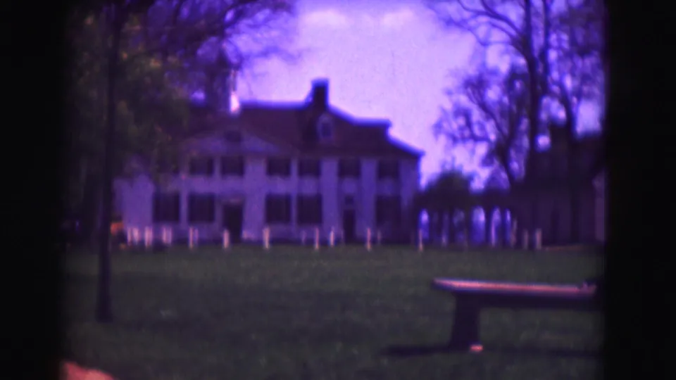 1975 Washington DC frame with an empty bench at lower right and a large white mansion across the grassy grounds.