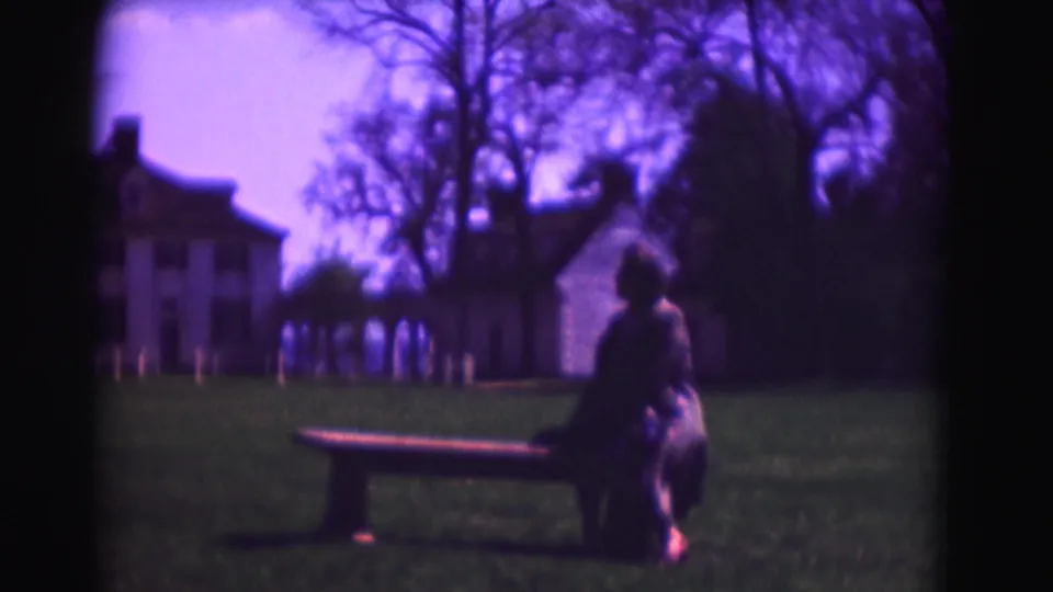 Soft 8mm view of a seated person on a lawn bench with white historic houses in Washington, DC, in the background.