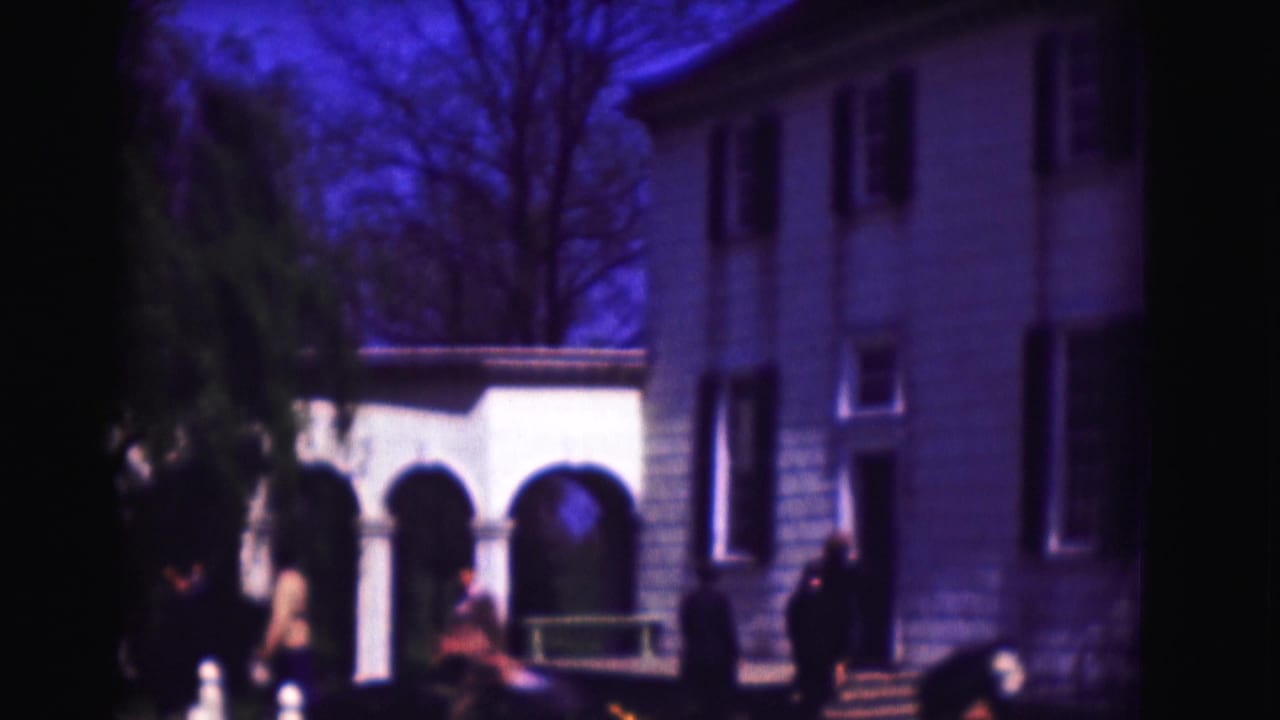 White house exterior with arched portico, bare trees, lawn, and several people near the entrance.