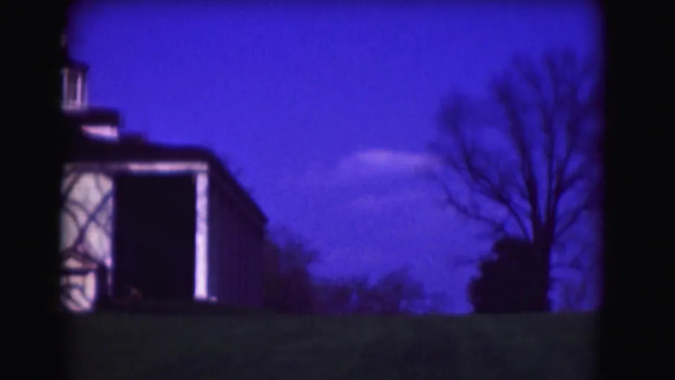 1975 8mm Washington, DC frame showing a white residence side view with cupola, lawn, bare trees, and a strong blue color cast.