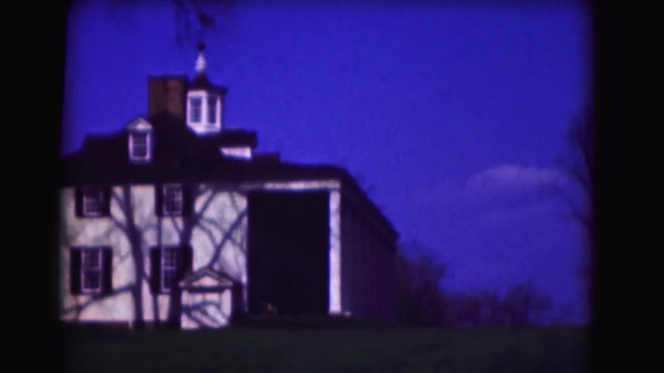 1975 8mm Washington, DC home-movie frame of a white building facade with cupola, shutters, lawn, and bare tree silhouettes.