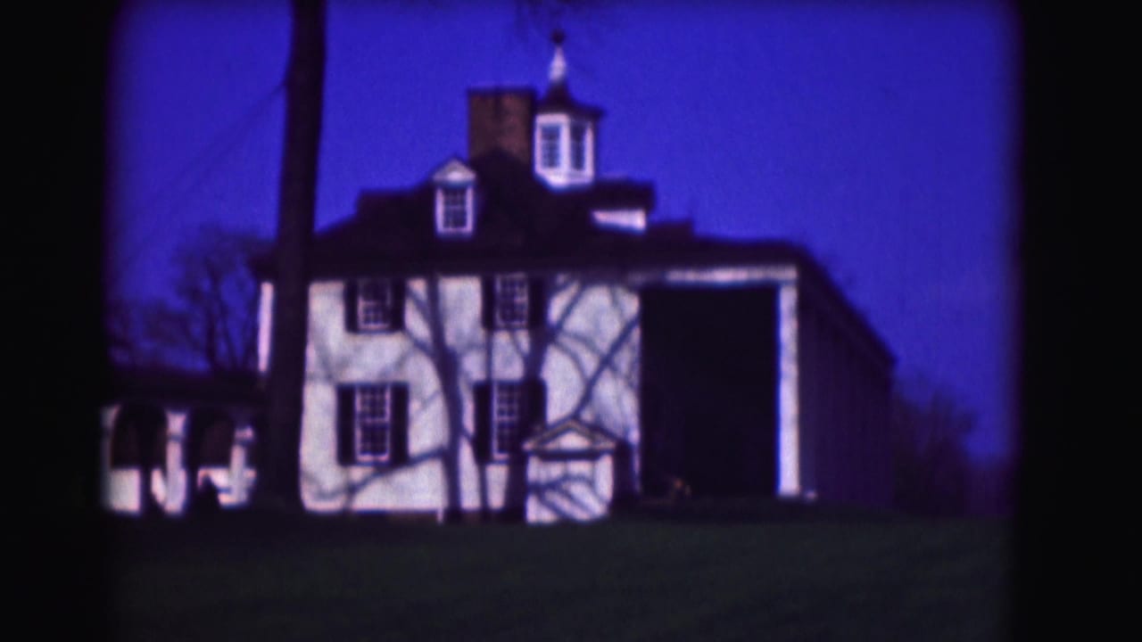 White two-story house with cupola, dark shutters, porch, lawn, and blue sky.
