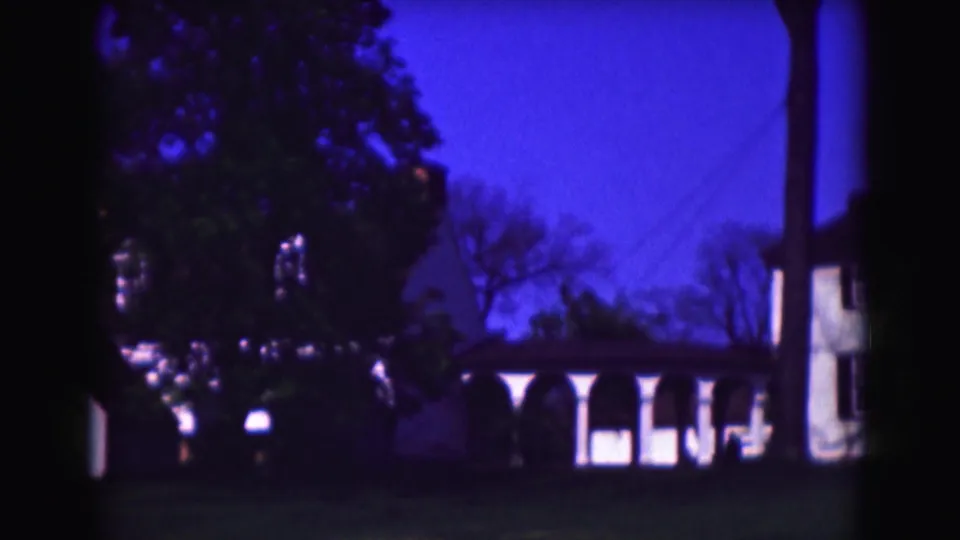 Soft 8mm frame from the 1975 Washington, DC clip, with trees, porch columns, lawn, and part of the white house visible.