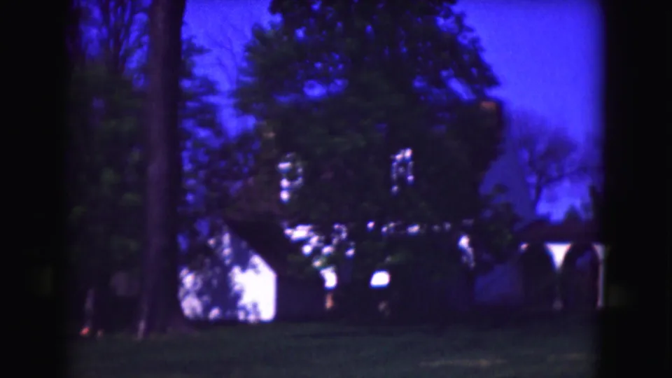 Washington, DC 1975 8mm frame with a dark tree, foliage, white building sections, porch columns, lawn, and blue sky.