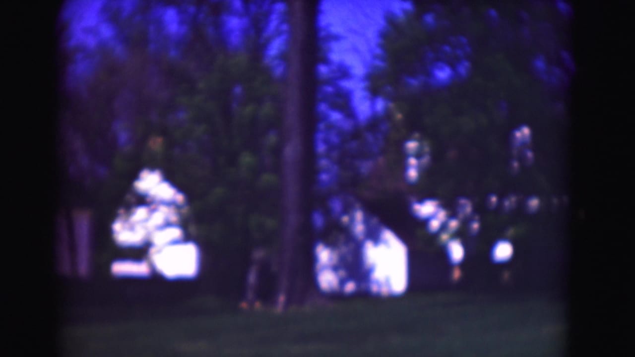 Soft 8mm view of trees, lawn, and bright white buildings beyond a dark foreground edge.