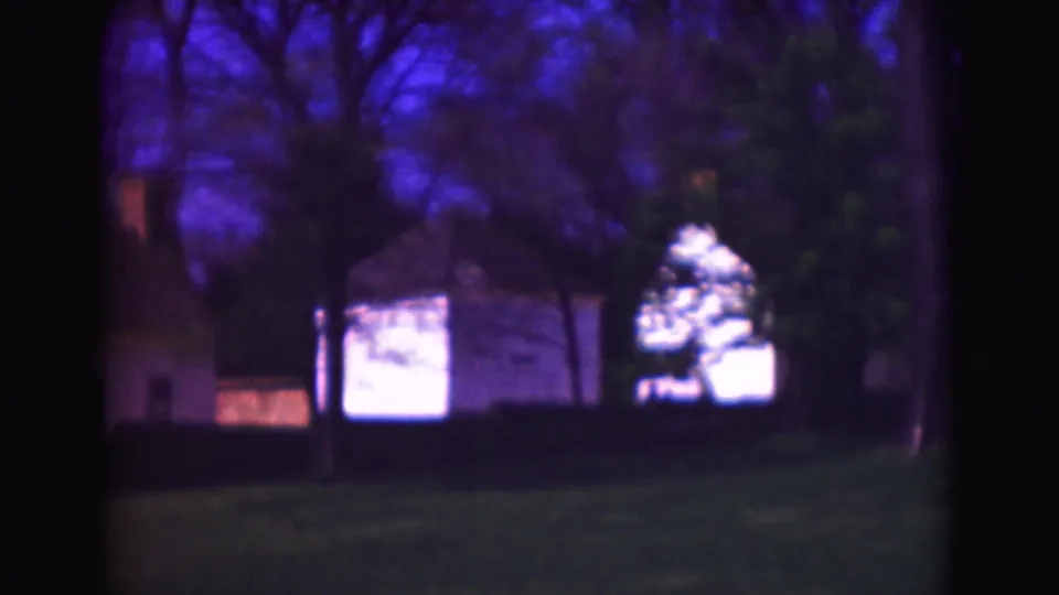 1975 Washington DC home-movie frame with trees, lawn, and historic-looking structures partly obscured by darkness and soft focus.