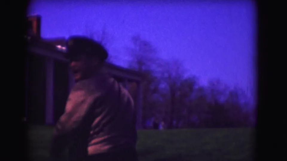 1975 Washington DC home-movie frame with a uniformed man in cap near a structure, seen in soft dusk-colored 8mm light.