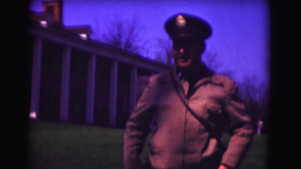 Uniformed adult man faces the camera in a soft 1975 Washington DC home-movie frame, with a columned building behind him.