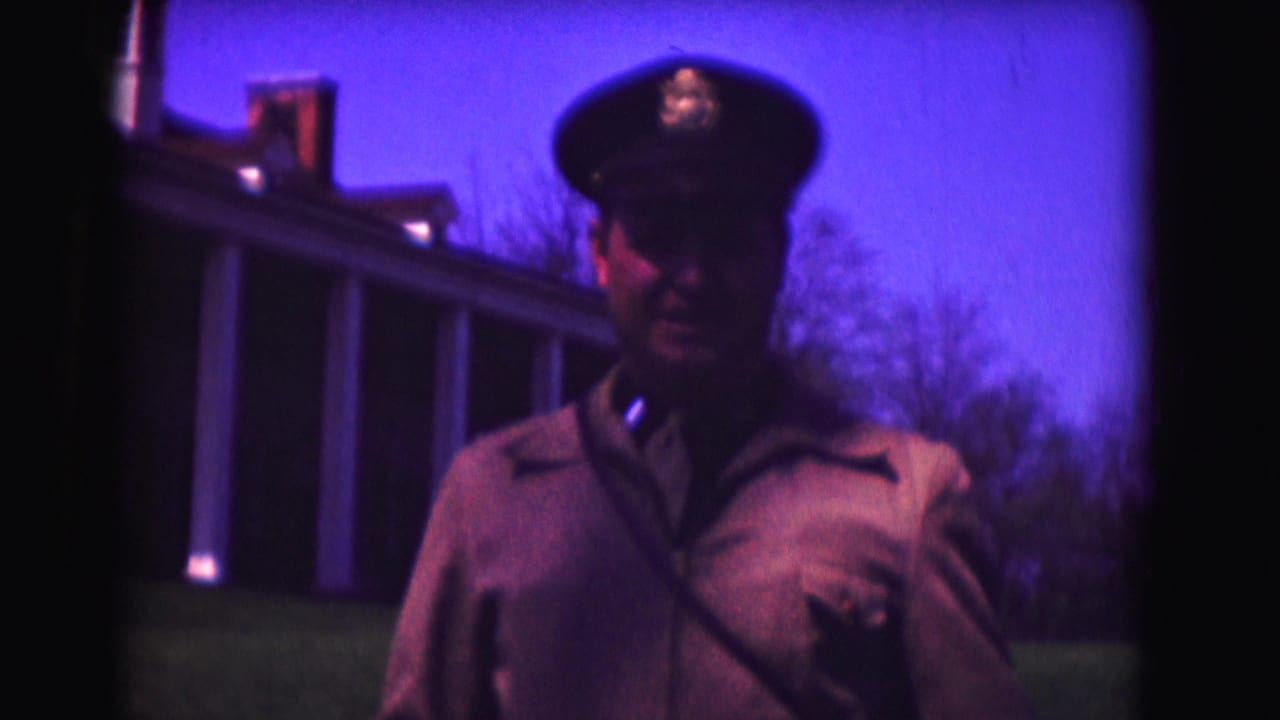 Closer view of a uniformed man in a peaked cap near a columned building.