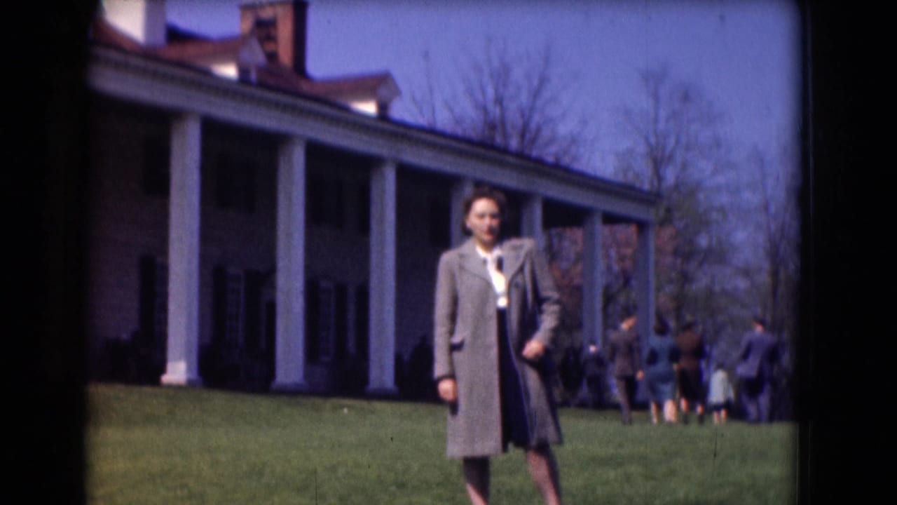 Woman in a gray coat walking on a lawn in front of a columned historic building.