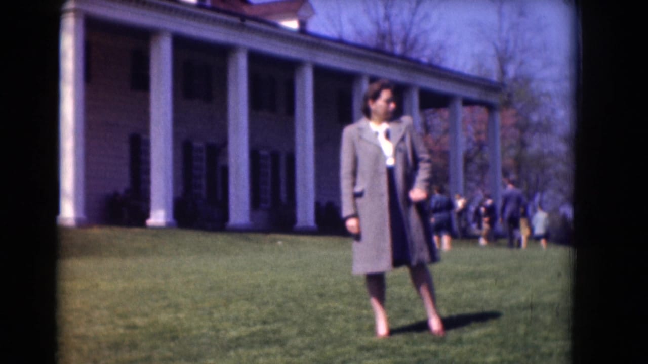 A woman stands on manicured grass in front of a grand white columned house during a 1975 Washington DC home-movie visit.