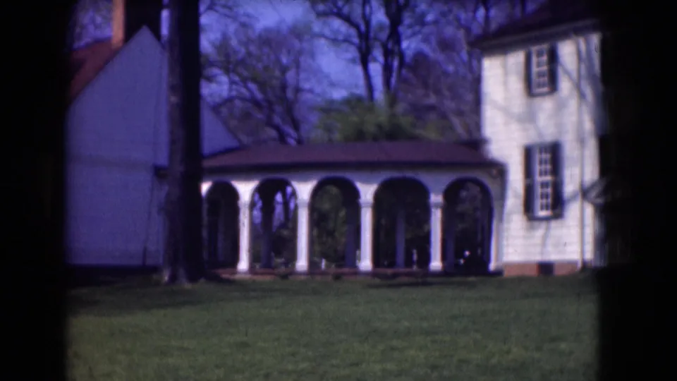 White historic-looking house and arched walkway seen across a lawn in Washington DC archival home-movie footage.
