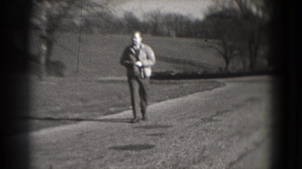 Adult man in a light jacket and dark pants walks along a paved path in a Washington, DC park-like setting, 1975 metadata supplied.