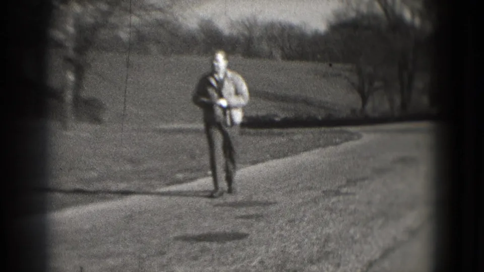 Adult man in a light jacket and dark pants walks along a paved path in a Washington, DC park-like setting, 1975 metadata supplied.