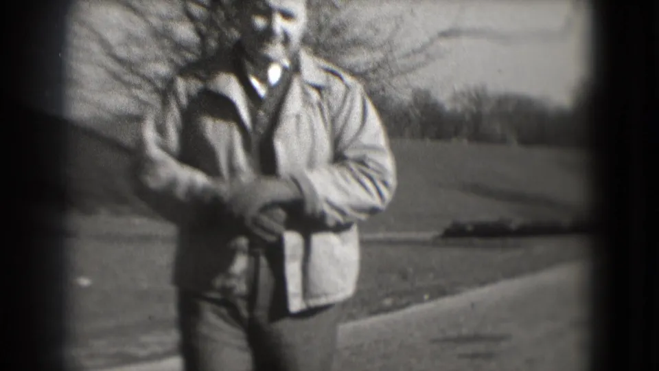A closer 1975 Washington, DC frame shows the man walking toward the camera, with a path, lawn, and bare trees in soft focus behind him.