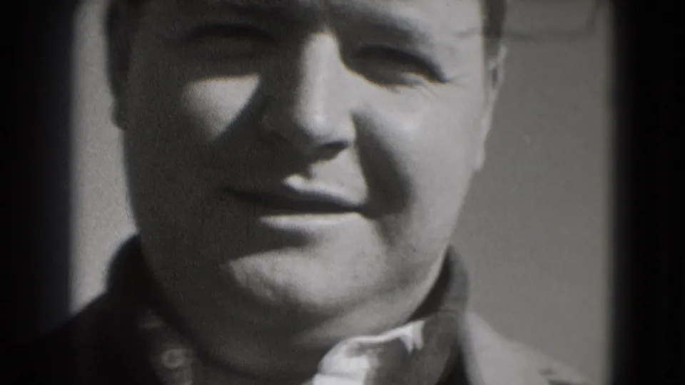 A close 8mm frame shows a smiling adult man, tightly cropped with soft exposure and visible film grain.