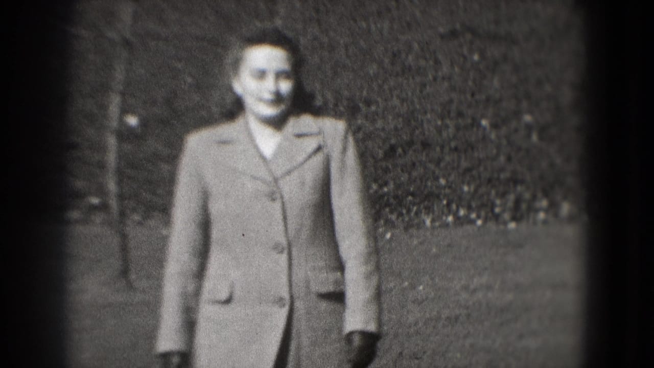 A smiling woman in a tailored coat walks toward the camera in a Washington, DC park setting, filmed on 8mm in 1975.