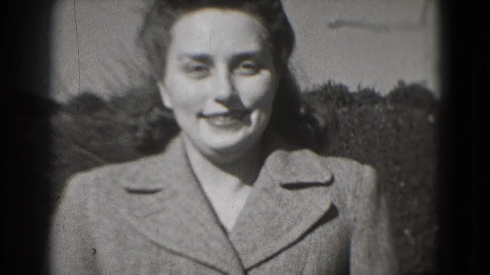 Young woman in a coat smiles directly at the camera in black-and-white 8mm footage from a Washington, DC home-movie context.
