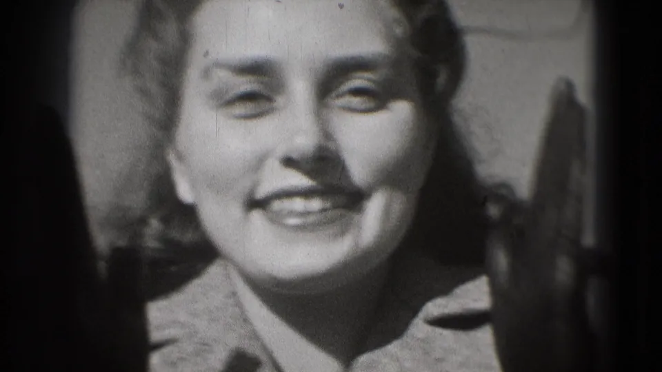 Close-up of a smiling woman in a coat, with heavy 8mm frame edges and soft black-and-white exposure.