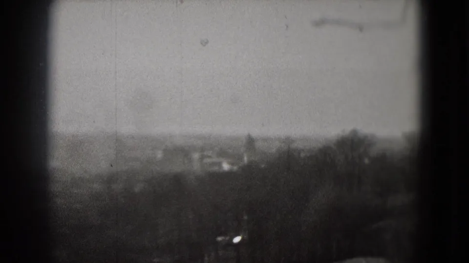 1975 Washington, DC home-movie frame showing a soft distant cityscape beyond dark trees and a pale sky.