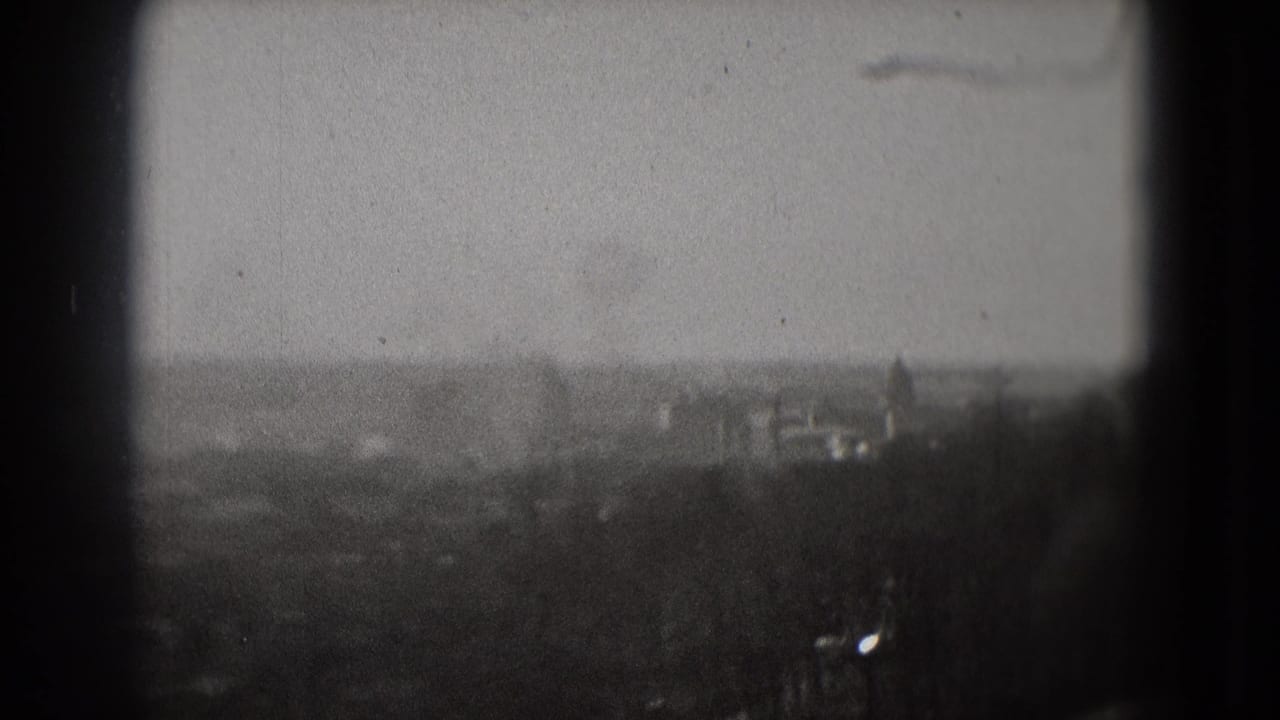 Soft 8mm view of Washington, DC from above, with distant buildings, treeline foreground, and dark film or window edges.