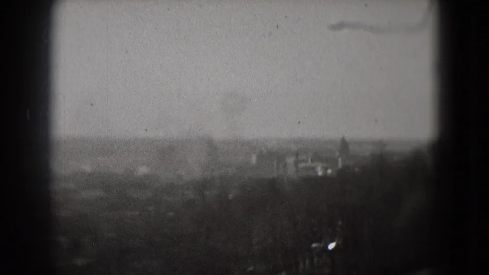 Soft 8mm view of Washington, DC from above, with distant buildings, treeline foreground, and dark film or window edges.