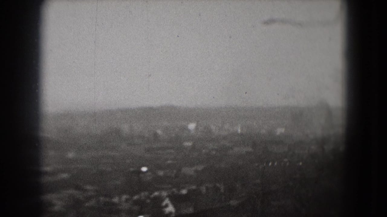 1975 Washington, DC home-movie frame showing a hazy distant city view and a small plane silhouette above the skyline.