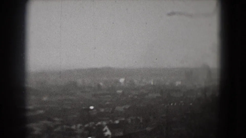 1975 Washington, DC home-movie frame showing a hazy distant city view and a small plane silhouette above the skyline.