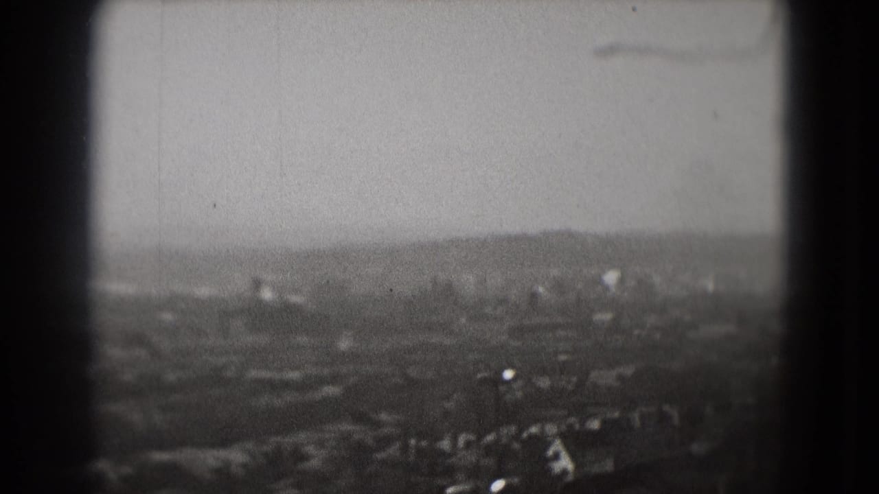 High-angle 1975 Washington, DC view with a plane visible against the hazy sky above distant buildings and roads.