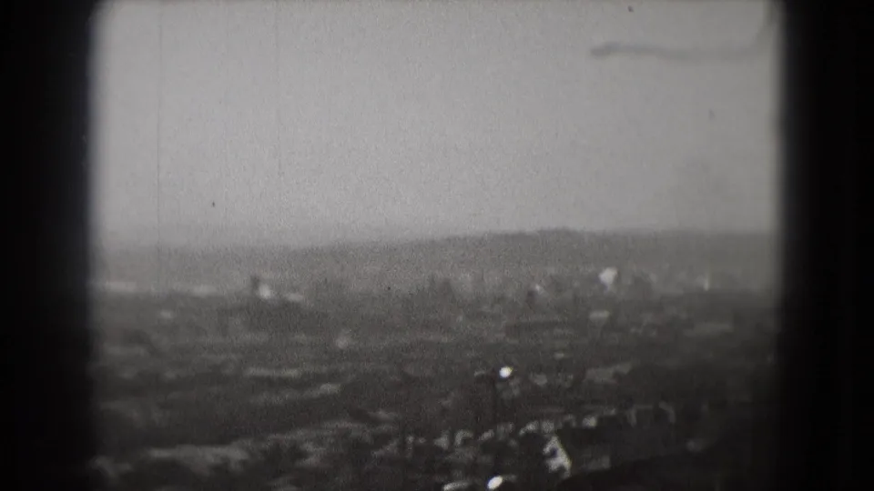 High-angle 1975 Washington, DC view with a plane visible against the hazy sky above distant buildings and roads.
