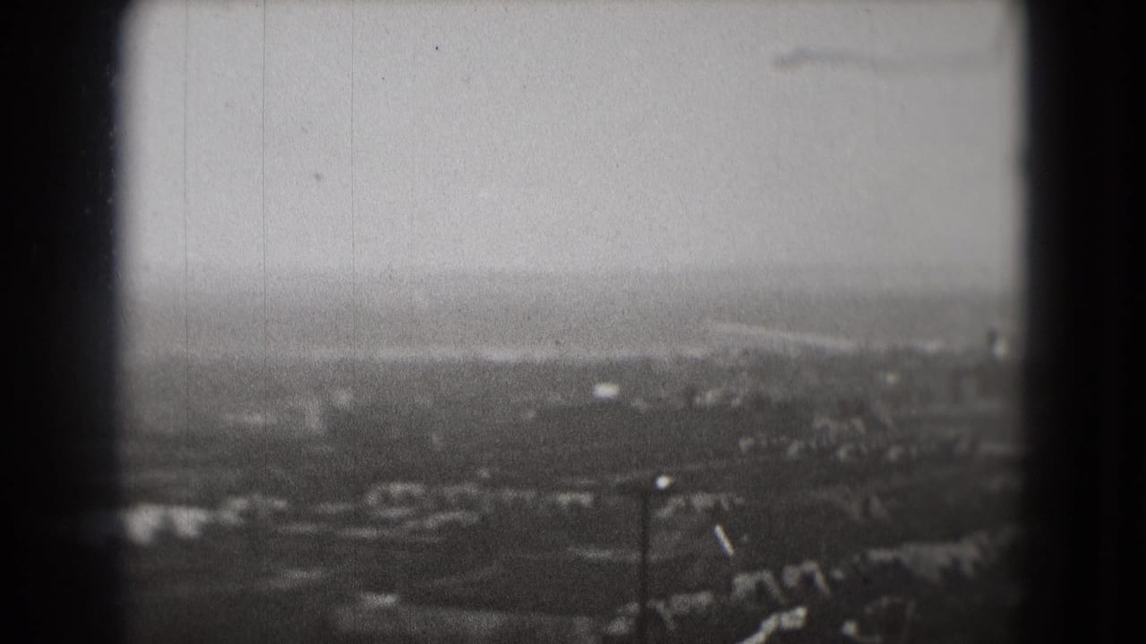 Soft aerial view of a hazy cityscape beneath a cloudy sky with dark film borders.