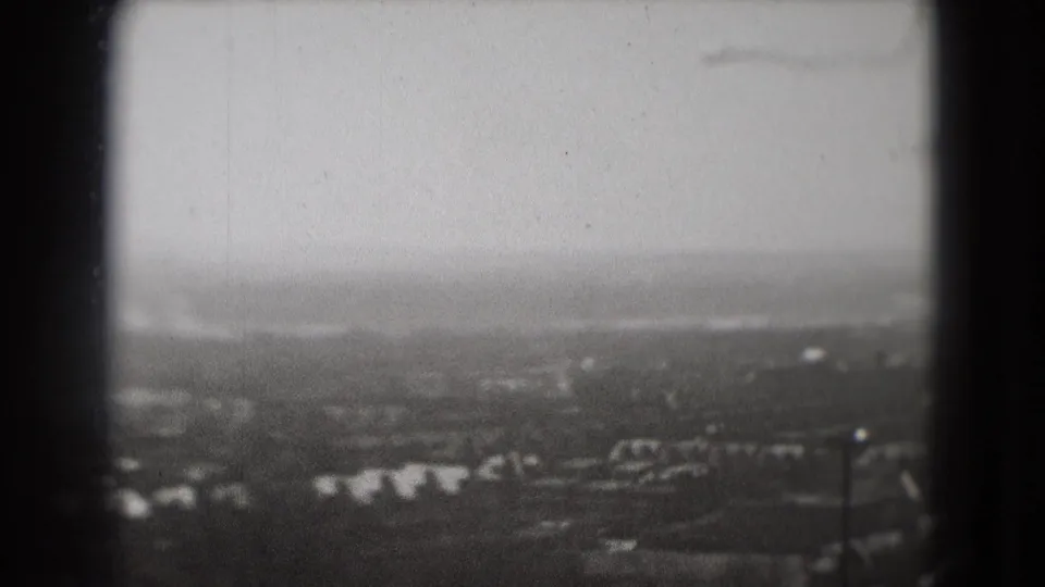 1975 Washington, DC aerial view with soft focus, distant structures, tree cover, cloudy sky, and prominent dark 8mm frame edge.