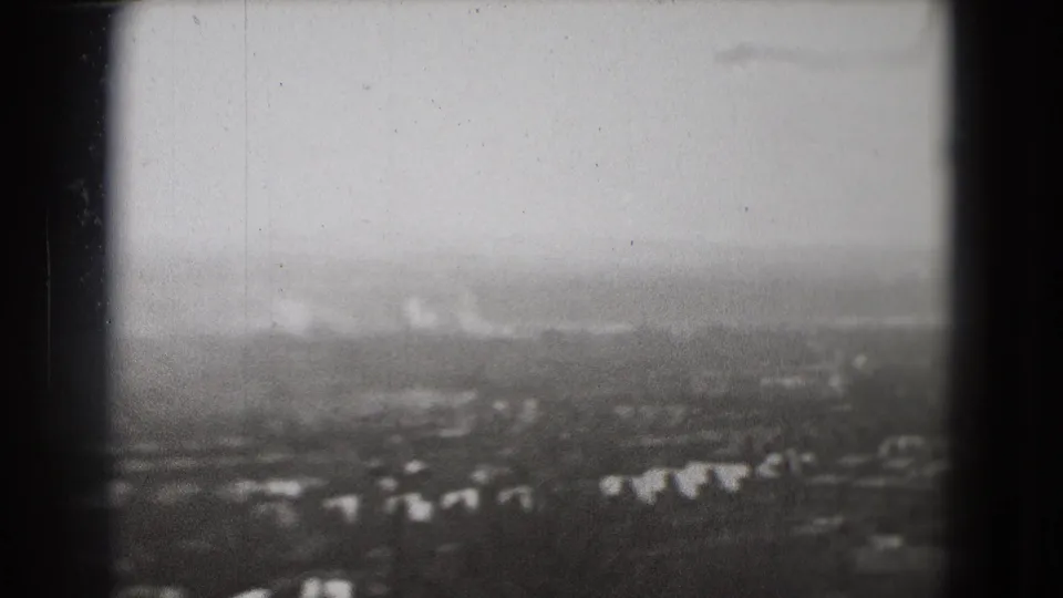 1975 Washington, DC home-movie aerial frame showing a blurred cityscape, scattered buildings, trees, cloudy sky, and visible film wear.