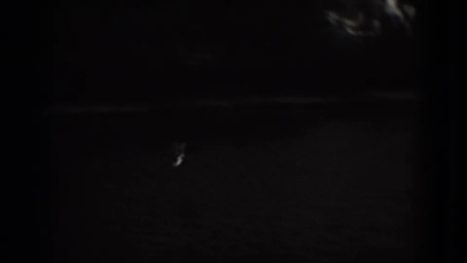 Dark 8mm frame from the Washington, DC aerial clip, with only faint ground detail, frame edges, grain, and dust visible.
