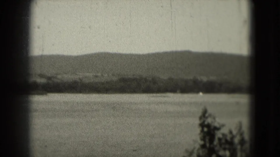 The final frame holds on a calm lake with distant hills, a low tree line, and foreground foliage in soft 8mm texture.