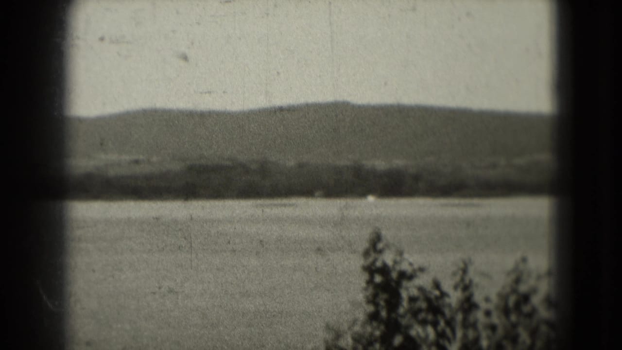 Calm river with distant tree-lined shore and low hills seen through dark film-frame borders.
