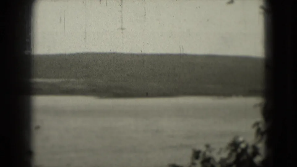 1975 home-movie frame showing a calm river below a distant Washington, DC area shoreline, with muted exposure and visible film wear.
