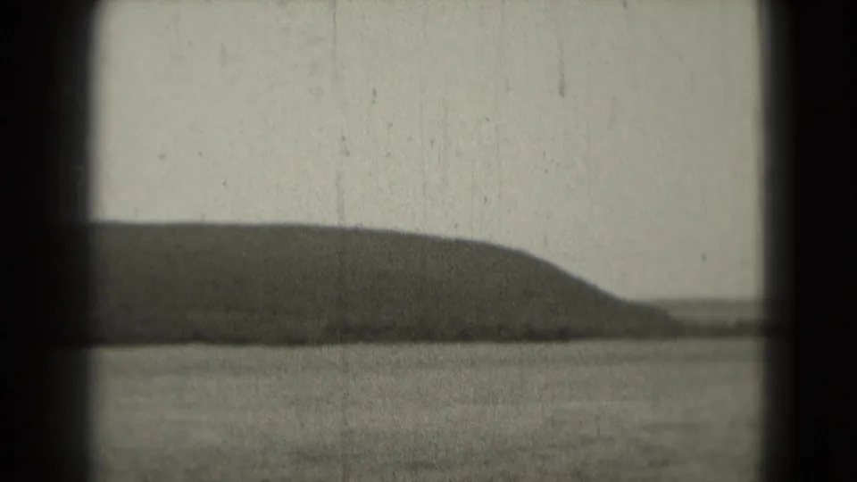 1975 8mm home-movie frame showing calm water and a low distant landmass, with dark film-gate edges and visible grain.