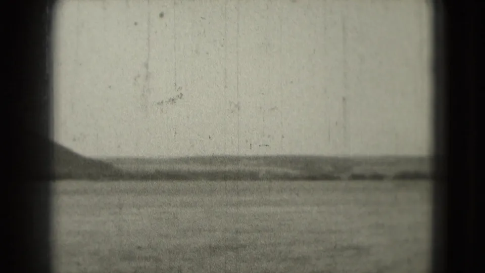1975 8mm frame of open water and a faint distant shoreline, with the landmass drifting toward the left edge during the pan.