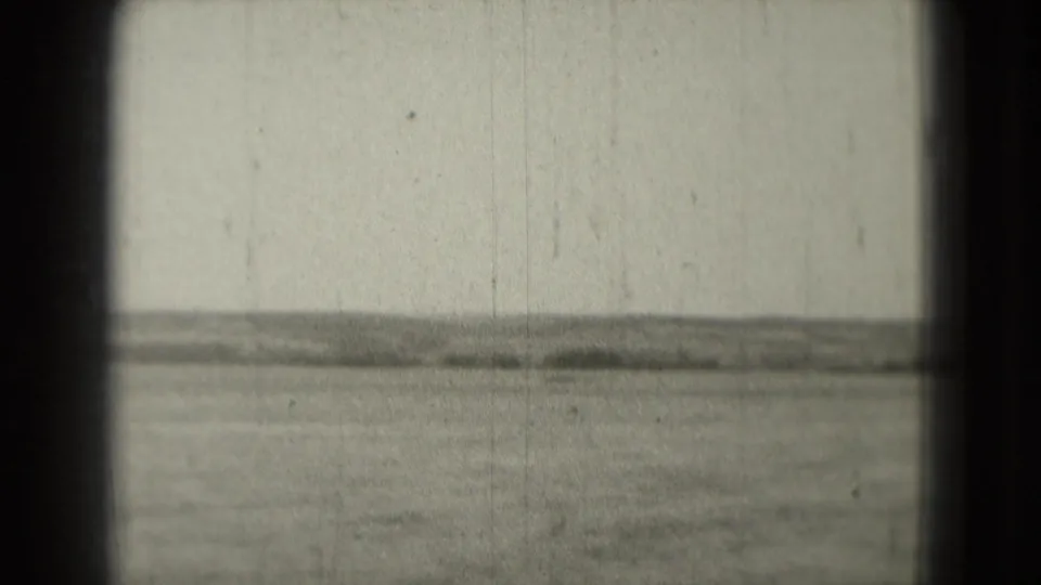 Grainy 1975 8mm view across water toward a faint low shoreline, with dark rounded frame edges and a soft horizon.