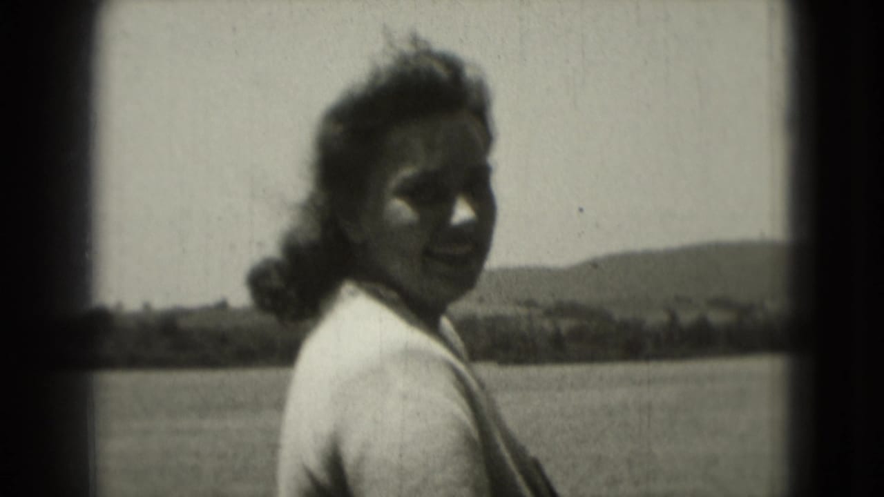 Woman outdoors turning toward the camera with windblown hair and distant hills behind her.