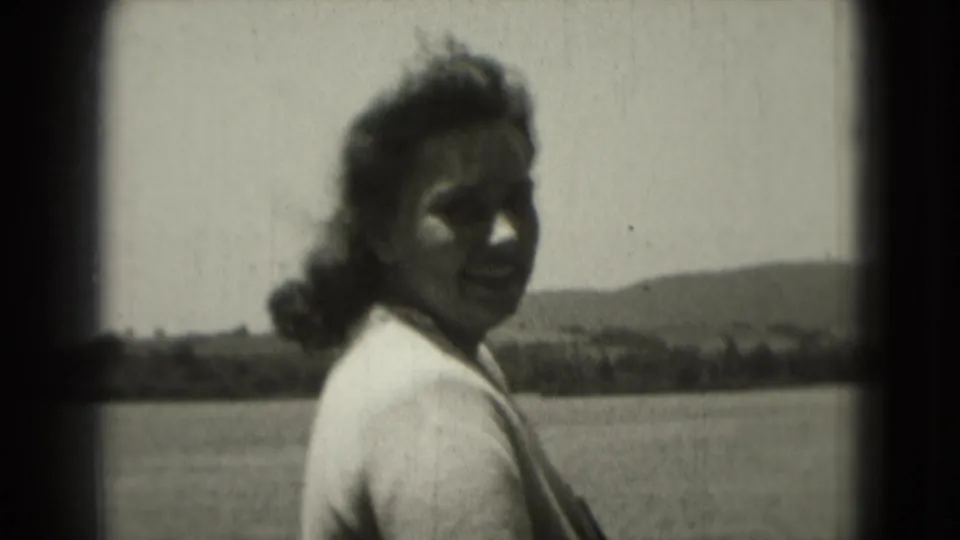 Adult woman in 1975 Washington DC home-movie footage turns toward the camera near an open landscape with distant hills.